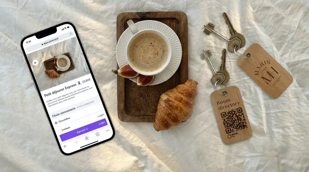 Porte-clefs hôtel bois en bambou gravé PIINK Me avec QR code Room directory, smartphone affichant l'interface de commande room service, café et croissant sur plateau en bois